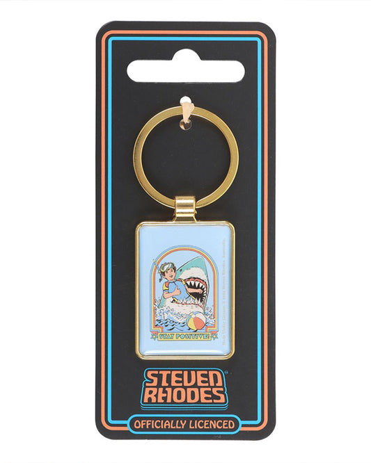 Rebel Romance Steven Rhodes Stay Positive enamel keyring displayed on official packaging. Retro humour snorkeller and shark artwork in gold frame. Officially licensed Steven Rhodes accessory for quirky alternative style lovers.