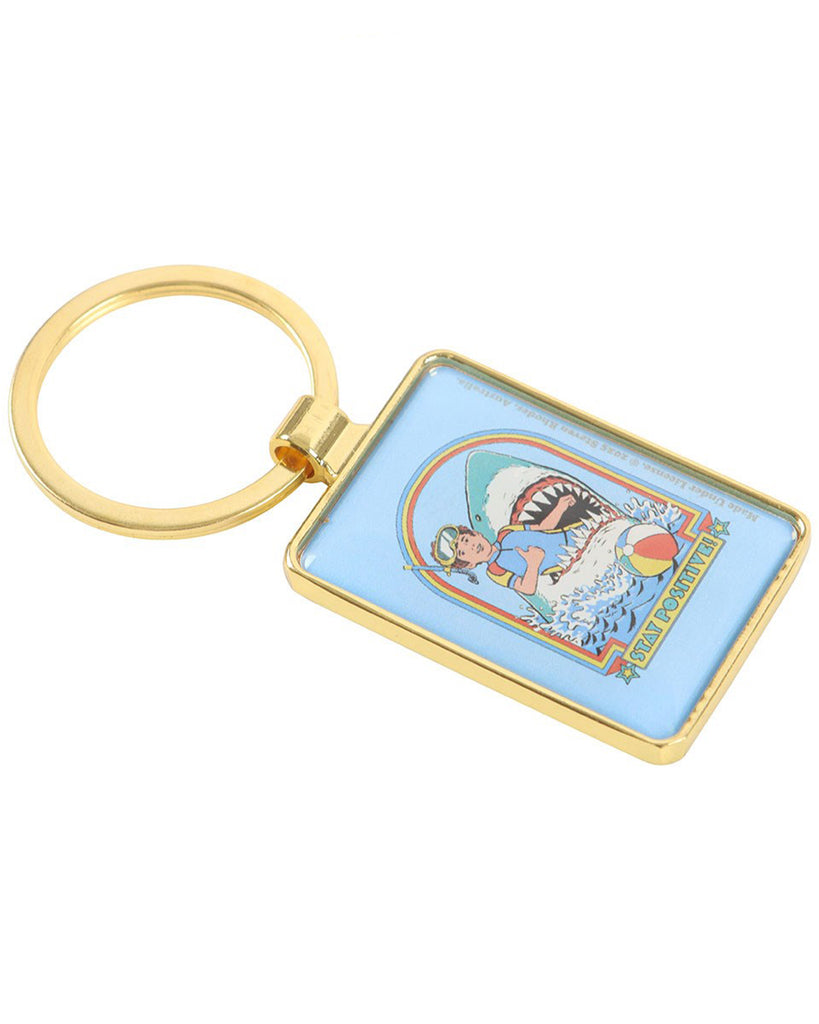 Angled view of the Rebel Romance Steven Rhodes Stay Positive enamel keyring with gold frame. Retro-style snorkeller and shark design with playful text, ideal for alternative fashion lovers and quirky gifts.