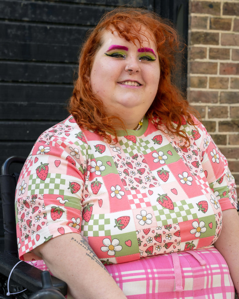 Model Lauren is wearing an XL Strawberry Picnic tee with bold green and pink makeup, styled with pink checked bottoms.