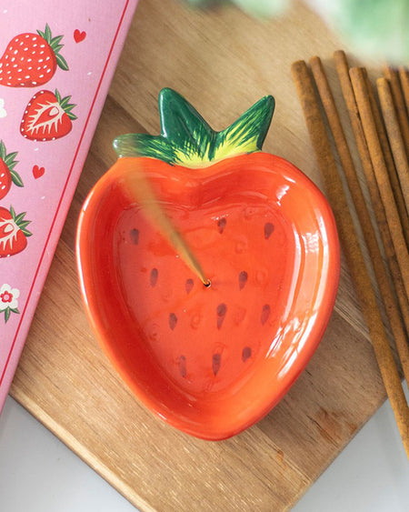 A styled shot of the strawberry incense holder on a wooden surface, surrounded by incense sticks and a strawberry-themed notebook. A perfect gift for fruity and retro décor lovers.