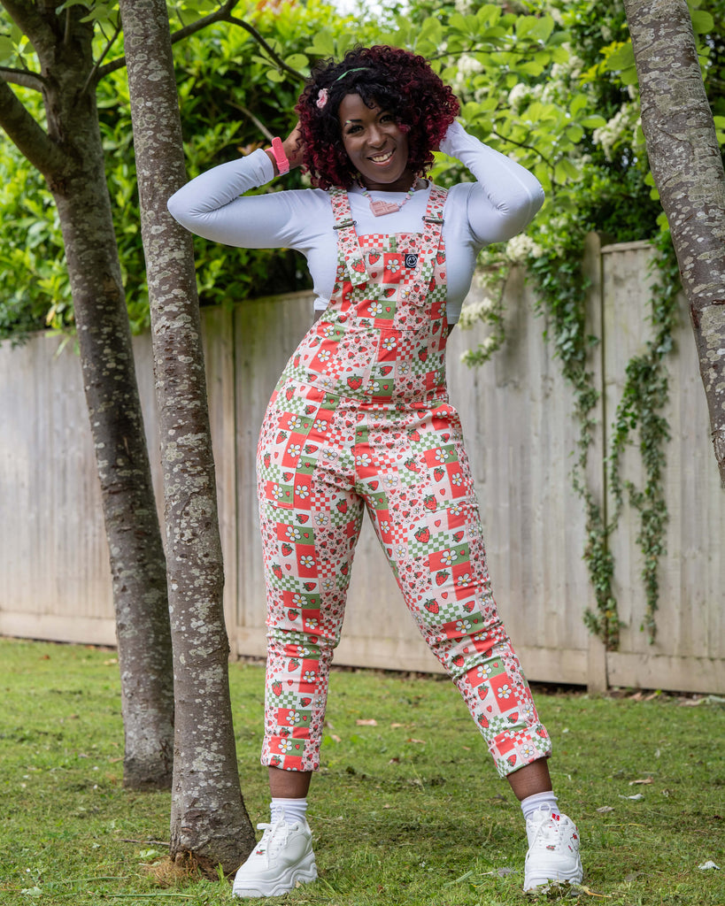 Ayesha poses confidently in the Rebel Romance Strawberry Picnic Stretch Dungarees, hands on head. The colourful fruit and flower print adds a playful twist to the fitted dungaree style. Styled with a long sleeve white crop top and chunky trainers.