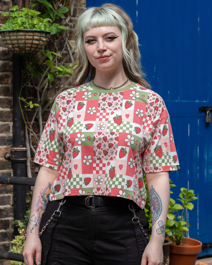 Front view of the cropped Strawberry Picnic tee by Rebel Romance, styled with black cargo trousers. The fun patchwork print features strawberries, daisies, hearts, and checkerboards.