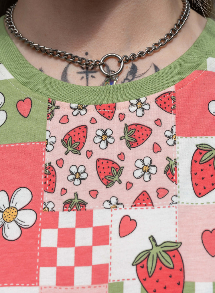 Detail shot of the green contrast neckline and patchwork print on the Strawberry Picnic cropped tee, featuring daisies and strawberries in pastel tones.
