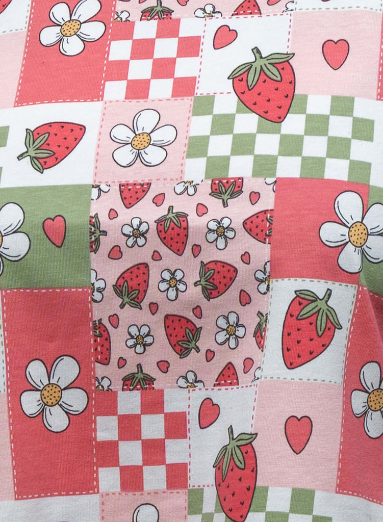 Close-up of the Strawberry Picnic print on Rebel Romance’s cropped boxy tee, showing red strawberries, white daisies, pink hearts, and green and red checkerboard panels.