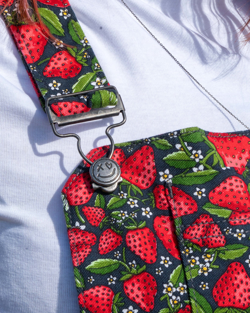Detailed view of the Rebel Romance Strawberry Field Pinafore bib, featuring metal fastenings.