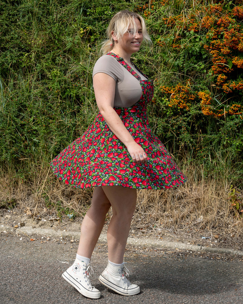 Harleigh twirls in the Rebel Romance Strawberry Field Flared Pinafore, a retro-inspired dress with a bold strawberry print, ethically made in India.