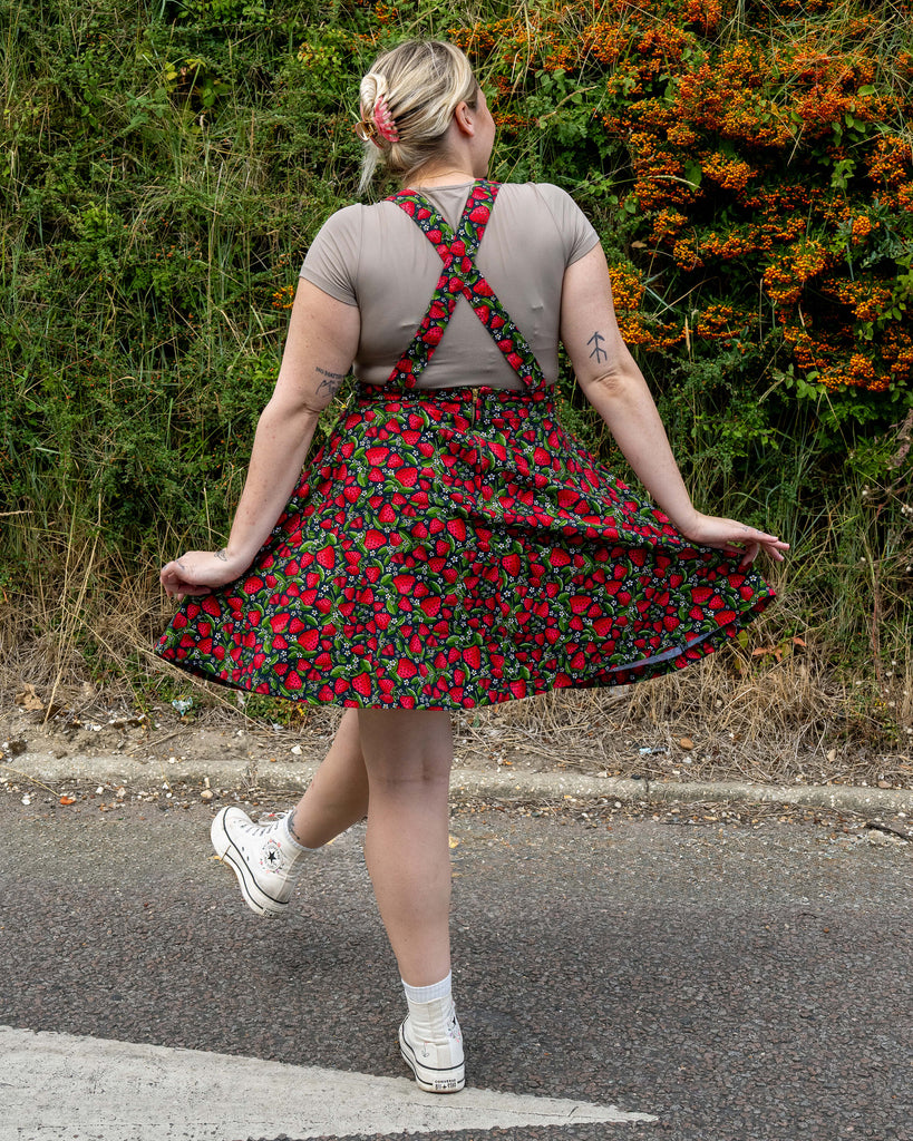 Back view of Harleigh wearing the Strawberry Field Flared Pinafore, showing the cross-over adjustable straps and gold zip fastening.
