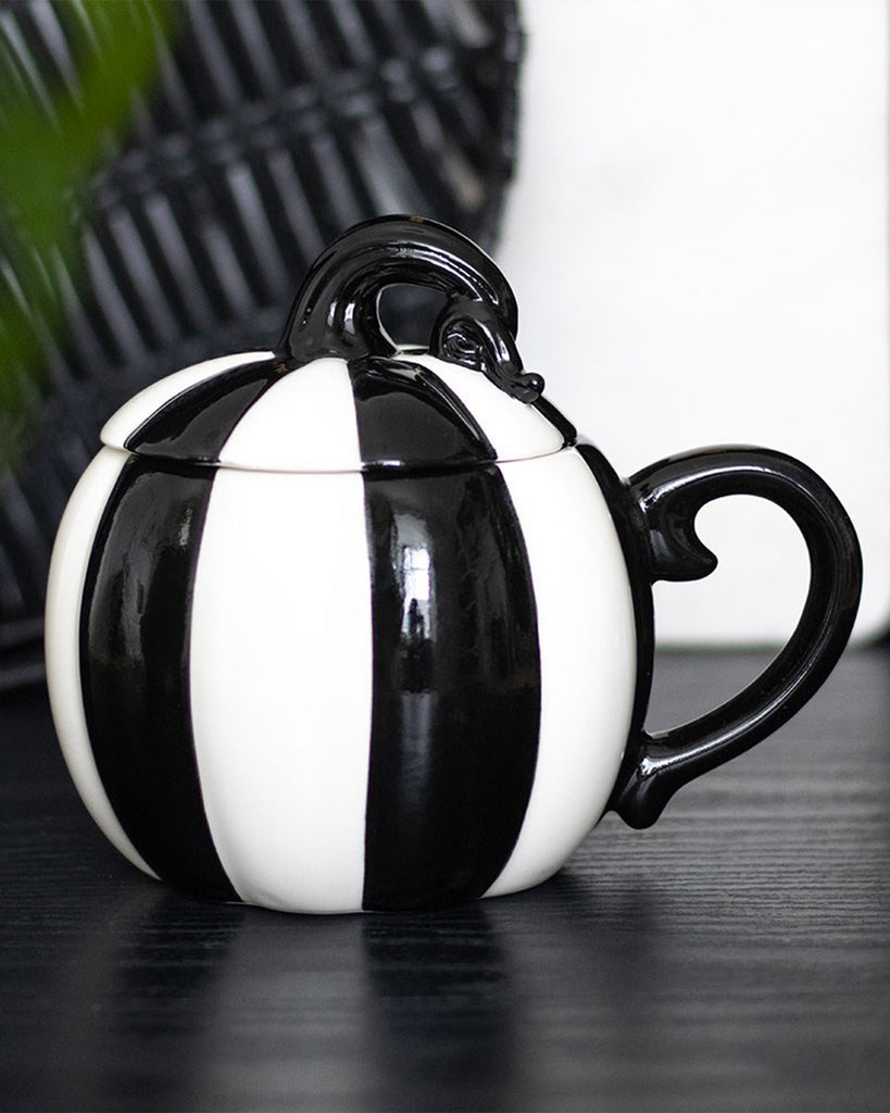Lifestyle shot of the Rebel Romance pumpkin mug on a black wooden surface, showing off its glossy ceramic stripes and vintage-inspired pumpkin shape. A perfect gothic gift or kitchen centrepiece.