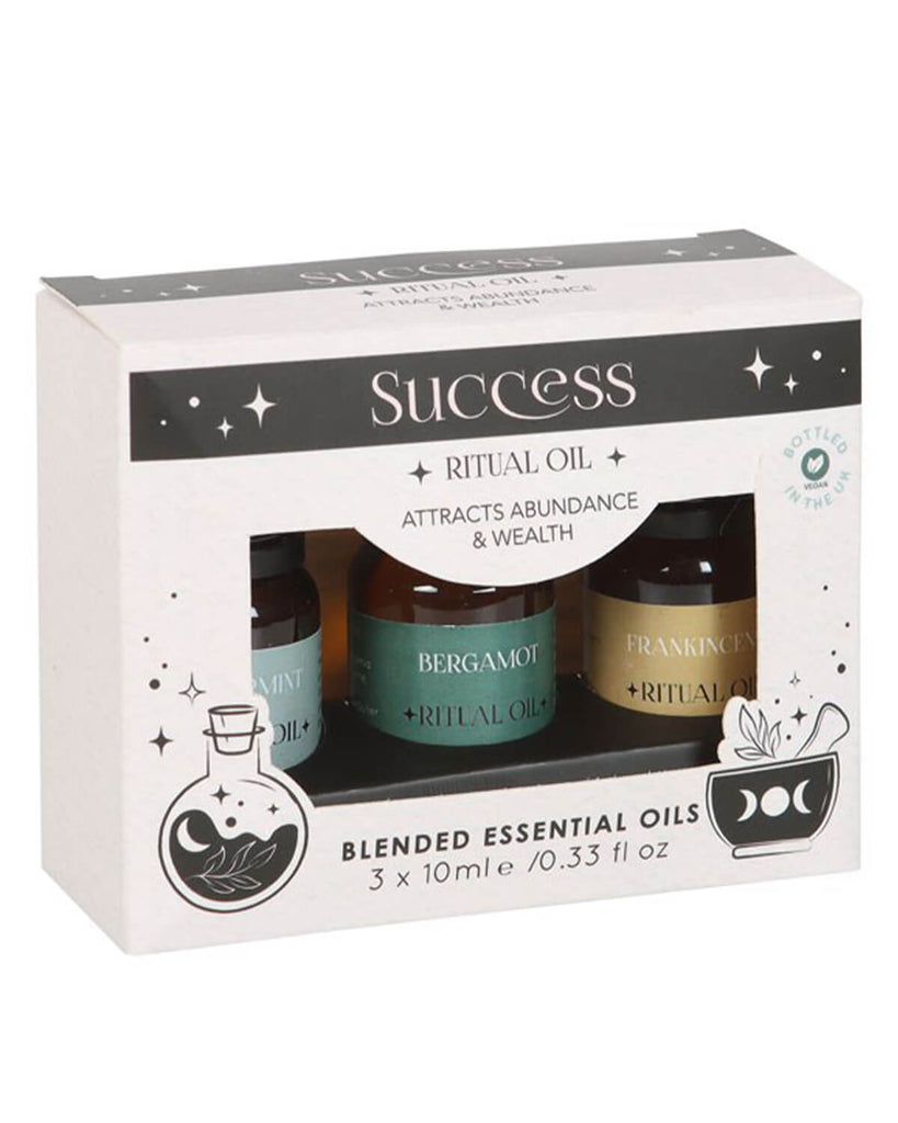 Side angle view of the Success Ritual essential oils box showing the front design and part of the bottles inside. The box has a white and black mystical theme with crescent moons and potion bottle illustrations.