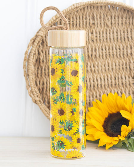 Rebel Romance sunflower glass water bottle styled with a natural woven backdrop and a real sunflower. The bottle's bright, cheerful print stands out, making it an ideal gift for anyone who loves bold, alternative style with eco-conscious flair.