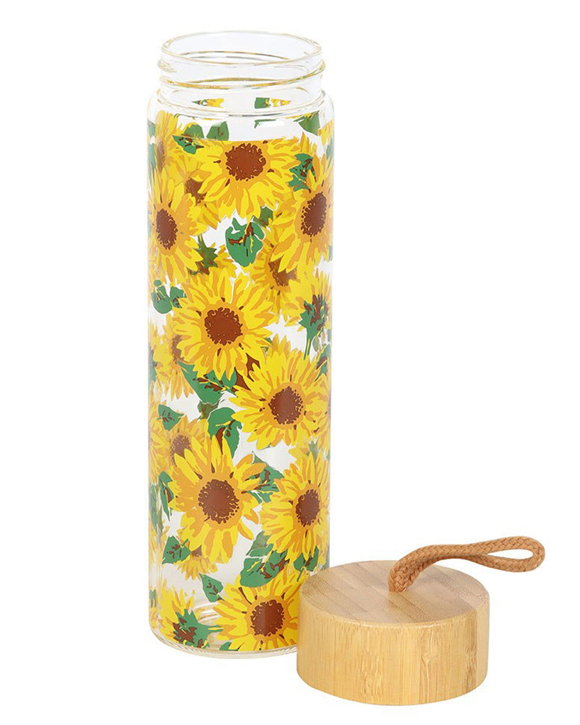 Open sunflower glass water bottle from Rebel Romance. The bamboo lid with its tan cord loop is placed beside the bottle, showing the wide mouth opening. The sunflower design wraps around the clear glass, creating a fun and functional eco-conscious accessory for millennials.