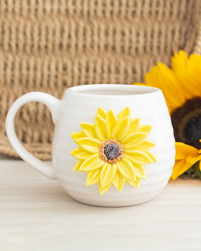 Close-up of the Rebel Romance Hello Sunshine rounded ceramic mug with a raised 3D sunflower design, styled with real sunflowers in the background for a bright and happy homeware vibe.