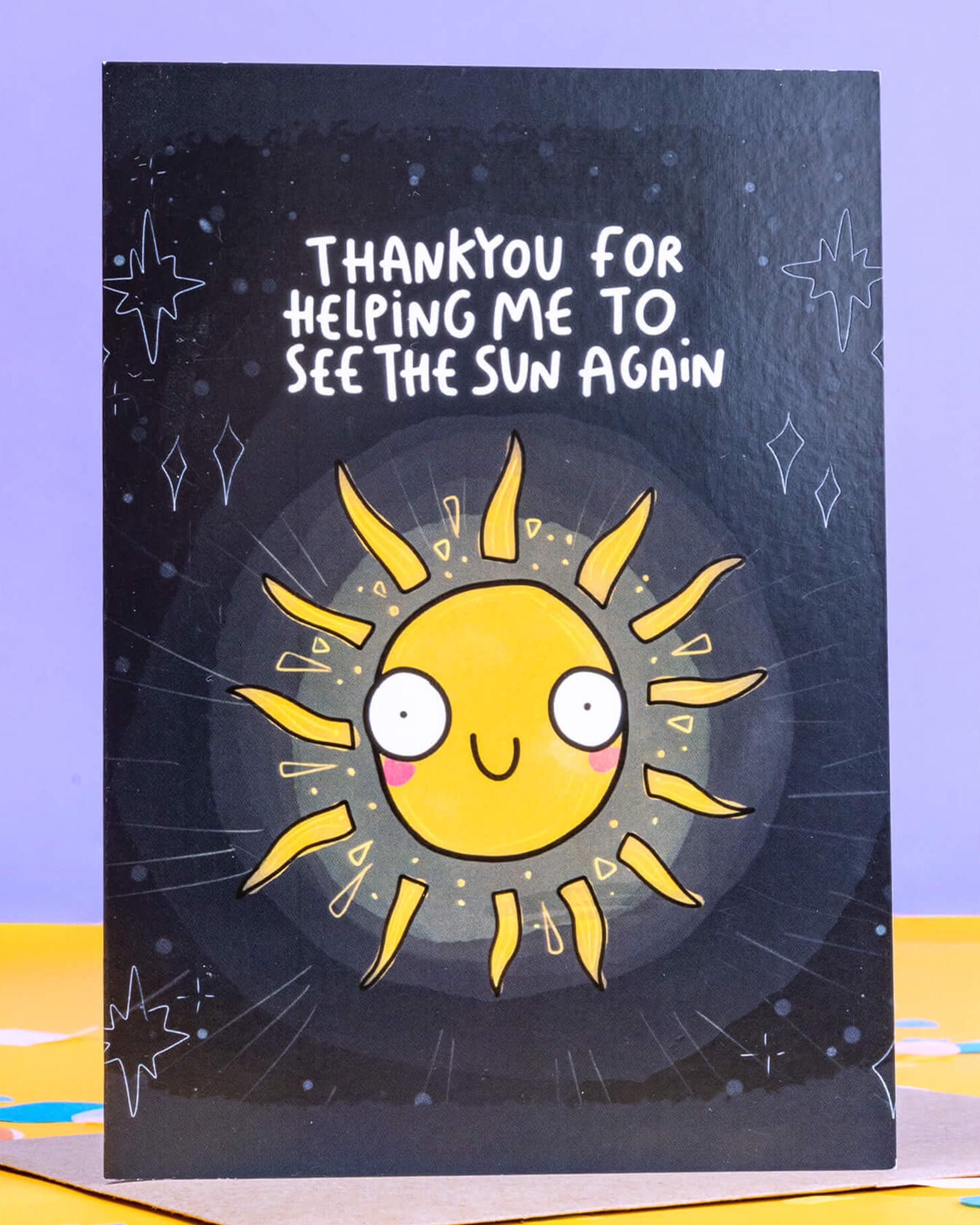 A6 greeting card from Rebel Romance featuring a bright, smiling cartoon sun with a cute face and rays against a dark sky. Surrounded by hand-drawn stars and sparkles, the card says “Thank you for helping me to see the sun again” in playful white text. A thoughtful and quirky illustrated card by Katie Abey, perfect for expressing gratitude. Designed in the UK by a small alternative brand celebrating unique style.