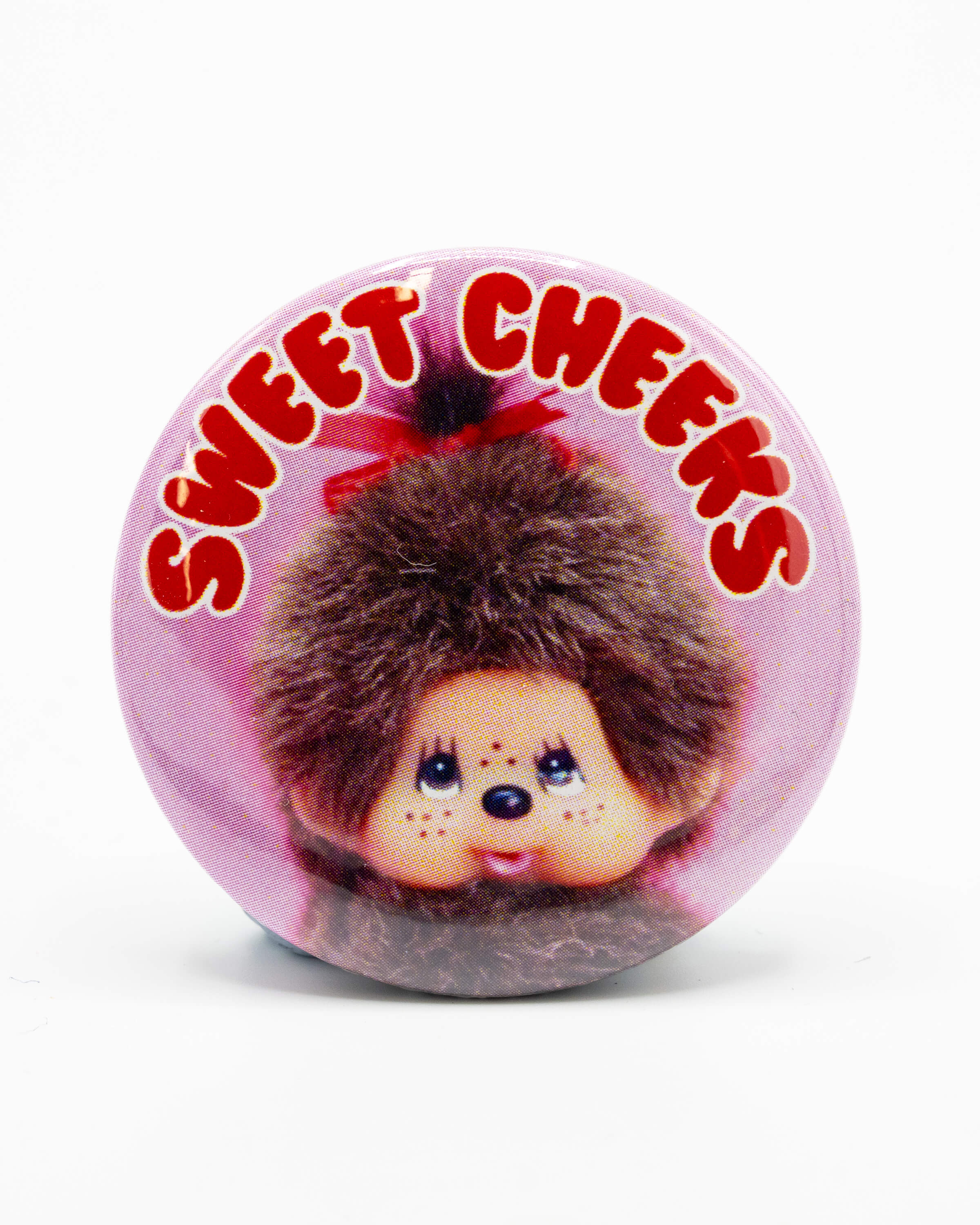 Button badge with a retro monchhichi monkey design and 'Sweet Cheeks' red bubble text on a pink background, an 80s retro design from Bite Your Granny.