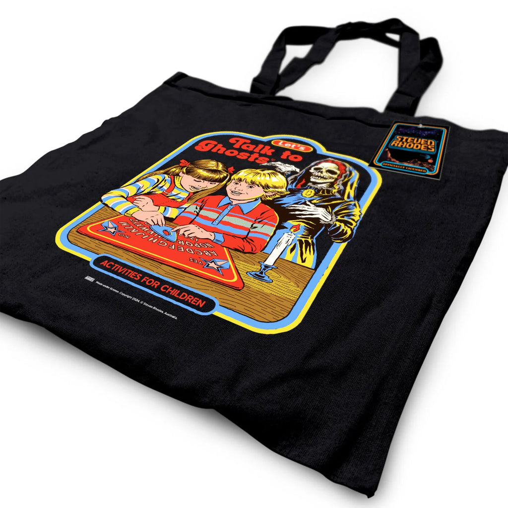 A black cotton tote bag featuring a retro-style Steven Rhodes design titled “Let’s Talk to Ghosts.” The illustration shows two children playing with a spirit board, with a skeleton ghost in the background. The vibrant design includes bold colours like red, yellow, and blue, paired with humorous text in a nostalgic comic-book style.