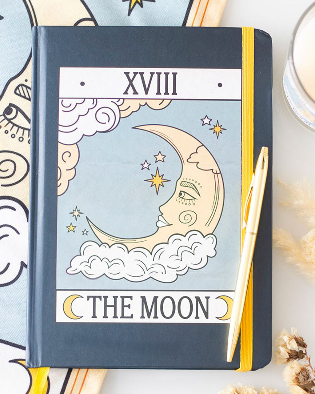 Flat-lay of The Moon tarot card-themed notebook on a white surface with dried flowers and a candle. The dreamy vintage design is perfect for astrology and tarot fans.