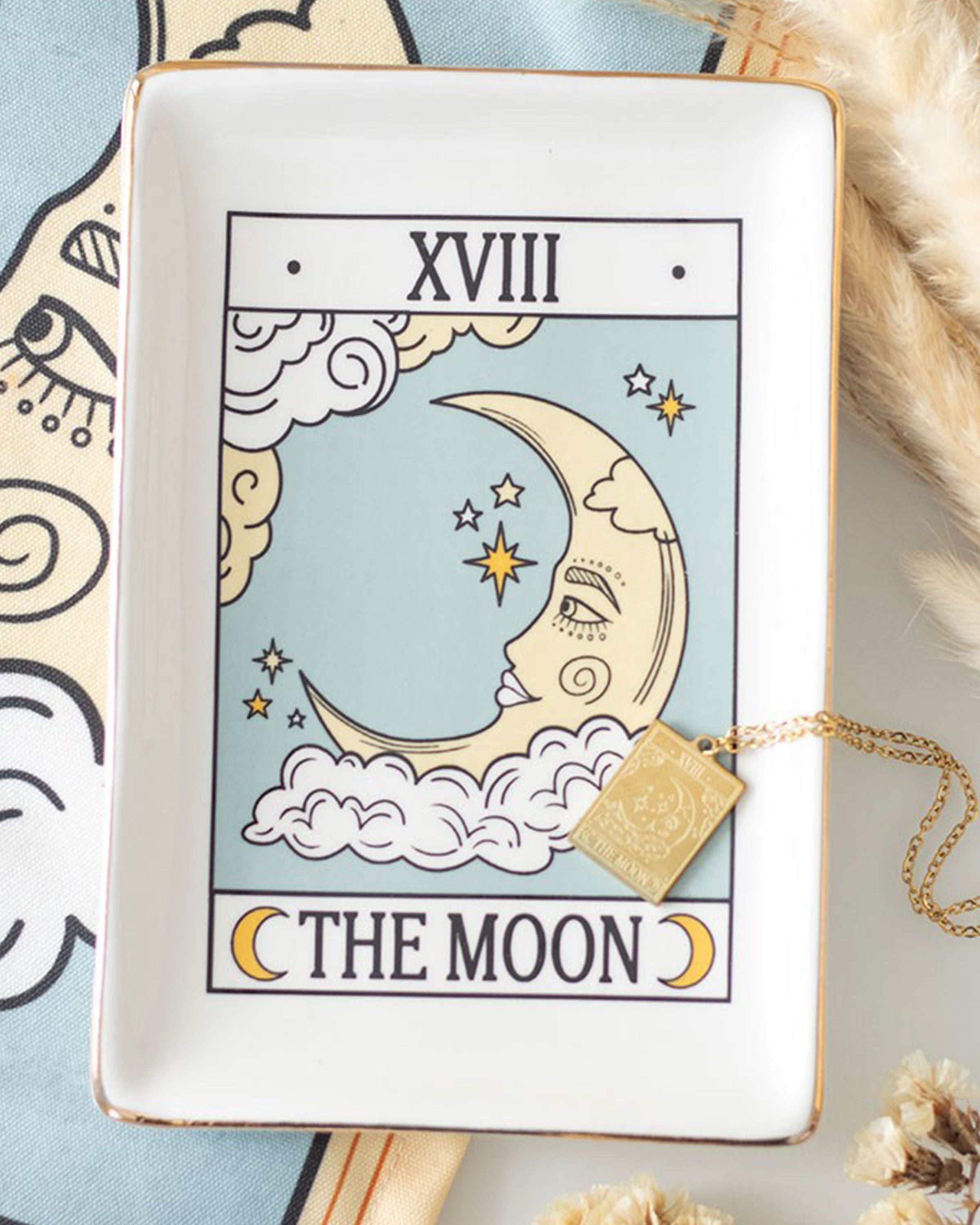 Ceramic trinket dish featuring The Moon tarot card design with gold edging, displayed with a gold necklace and celestial-themed cloth in the background.