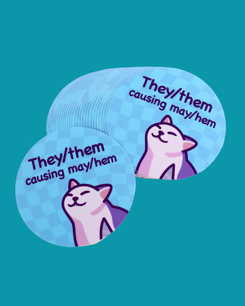 Round vinyl sticker with a blue chequered background and a smug cartoon cat illustration. Features the punny text “They/them causing may/hem” in bold lettering. A fun non-binary pride sticker that celebrates gender identity with humour. Designed by Mona Mauve and sold by Rebel Romance, a UK-based small business championing inclusivity and queer joy.