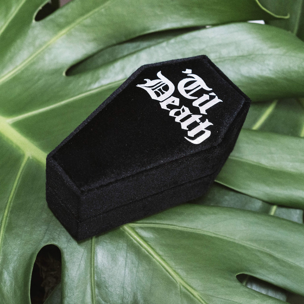 Coffin Shaped Ring Box - Til Death Closed
A black velvet coffin-shaped ring box with “Til Death” printed in gothic white font on the lid. Set against lush green leaves for a dramatic gothic aesthetic.
