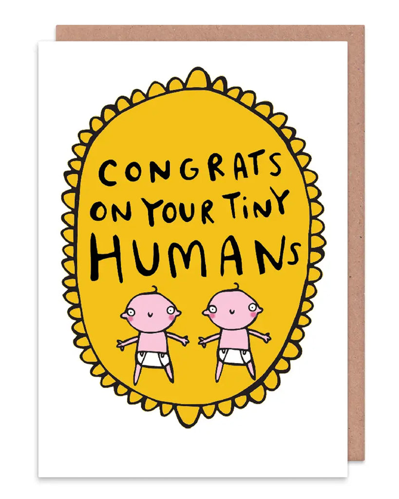 Congrats on your tiny humans A6 greeting card designed by Katie Abey and printed in the UK. The card is a white background with a gold frilly frame shape with two cartoon white babies and text above that reads 'congrats on your tiny humans'. Available on Rebel Romance