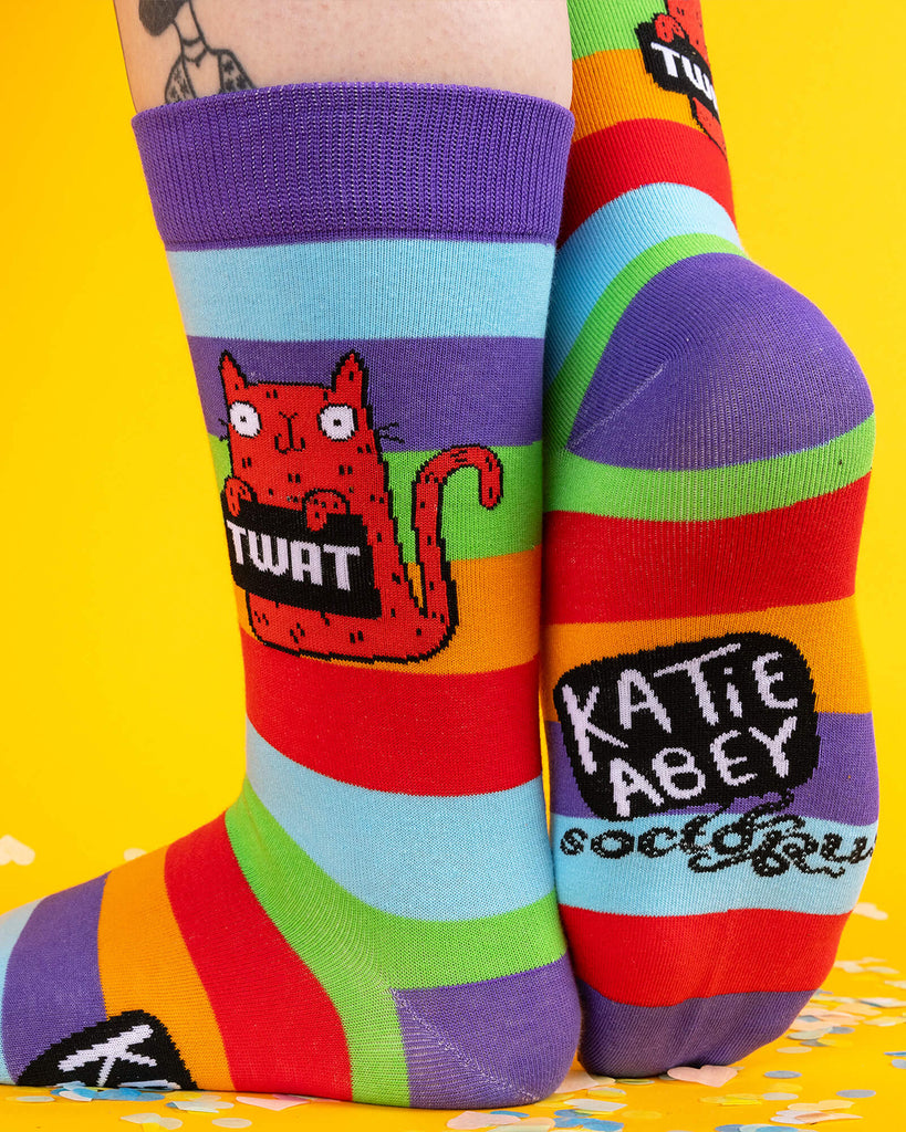 Back view of the socks worn on feet, showing one sole with the “Katie Abey” logo and the other with the red sweary cat design. Colourful and cheeky, perfect for gifting with attitude.