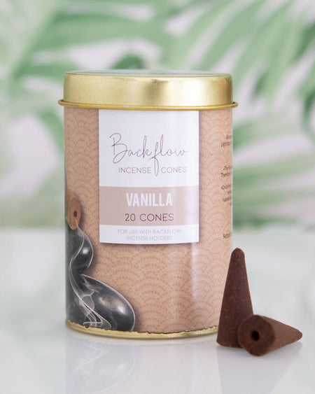 Styled image of the Elements Vanilla Backflow Incense Cones tin on a glass surface with a soft green leaf-patterned background, with two cones placed neatly in front.