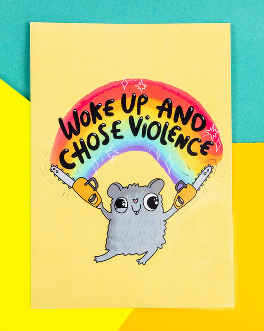A bright A6 postcard featuring a cartoon grey hamster holding two yellow chainsaws under a rainbow with the words “Woke Up and Chose Violence” above. Designed by Katie Abey and sold by Rebel Romance, this quirky illustration is printed on high-quality silk-finish card and makes a bold, humorous gift or wall display.