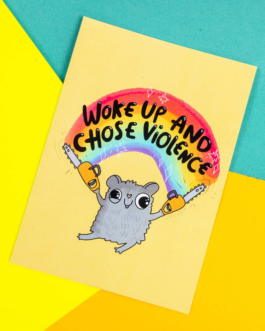 A bright A6 postcard featuring a cartoon grey hamster holding two yellow chainsaws under a rainbow with the words “Woke Up and Chose Violence” above. Designed by Katie Abey and sold by Rebel Romance, this quirky illustration is printed on high-quality silk-finish card and makes a bold, humorous gift or wall display.