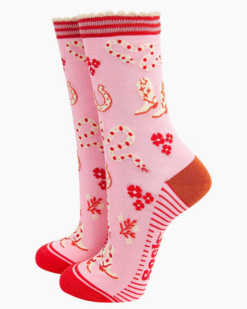 A pair of pink bamboo socks with a wild west theme featuring cowboy boots with heart details, red and cream rattlesnakes, horseshoes, and floral accents. The socks have a striped scalloped cuff, a burnt-orange heel, and red toes.