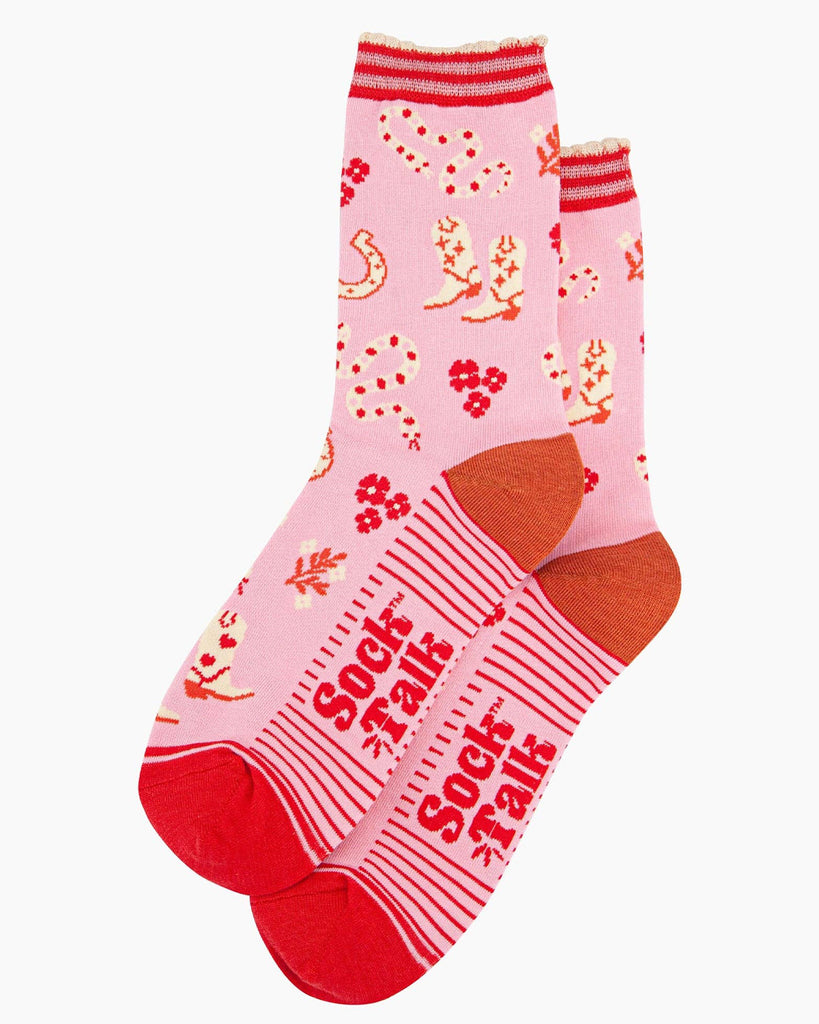 A pair of pink bamboo socks with a wild west theme featuring cowboy boots with heart details, red and cream rattlesnakes, horseshoes, and floral accents. The socks have a striped scalloped cuff, a burnt-orange heel, and red toes.