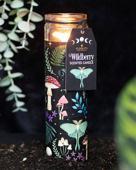 A lit Wildberry tube candle, placed in an earthy setting with ferns and dark soil, radiating an enchanted, magical atmosphere.