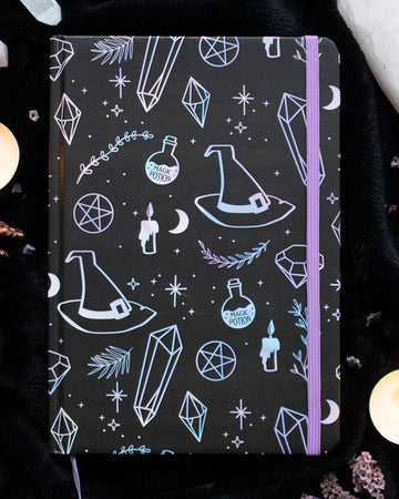 A5 black witchy notebook with holographic pastel illustrations of crystals, potion bottles, moons, and stars. Surrounded by candles and crystals, perfect for spiritual journaling or note-taking.