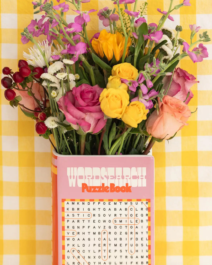 Rebel Romance Word Search Puzzle Book Vase styled with a bright bouquet of roses and wildflowers on a yellow gingham tablecloth, perfect for dopamine décor lovers.