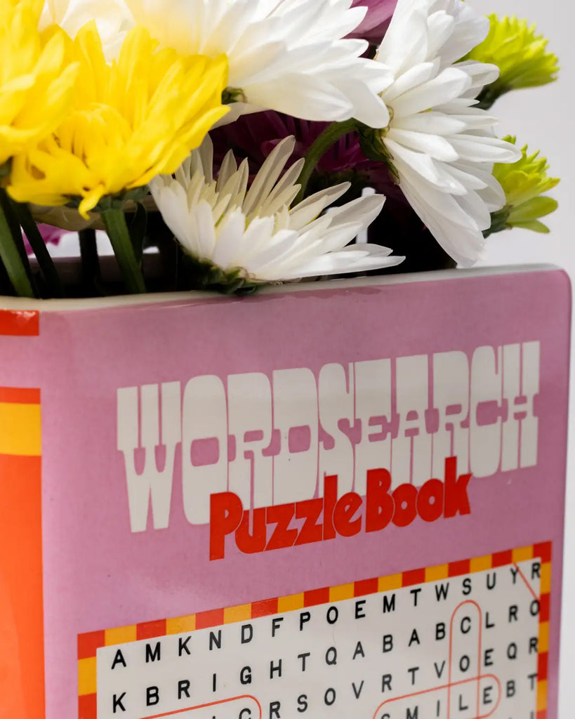 Detail shot showing the playful design of the Rebel Romance ceramic vase, shaped like a retro puzzle book and filled with daisies in vibrant colours.