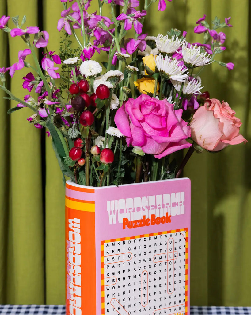 Floral arrangement featuring roses, daisies and berries in the Rebel Romance word search puzzle book vase, styled with green curtains and bold colours for a maximalist vibe.