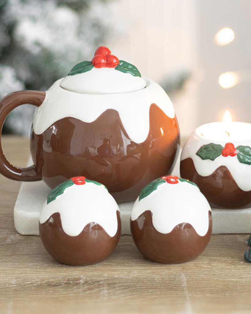 Festive Christmas pudding teapot and salt and pepper shakers set on a wooden table with candle and holly decorations. Perfect for a cosy holiday table setting.