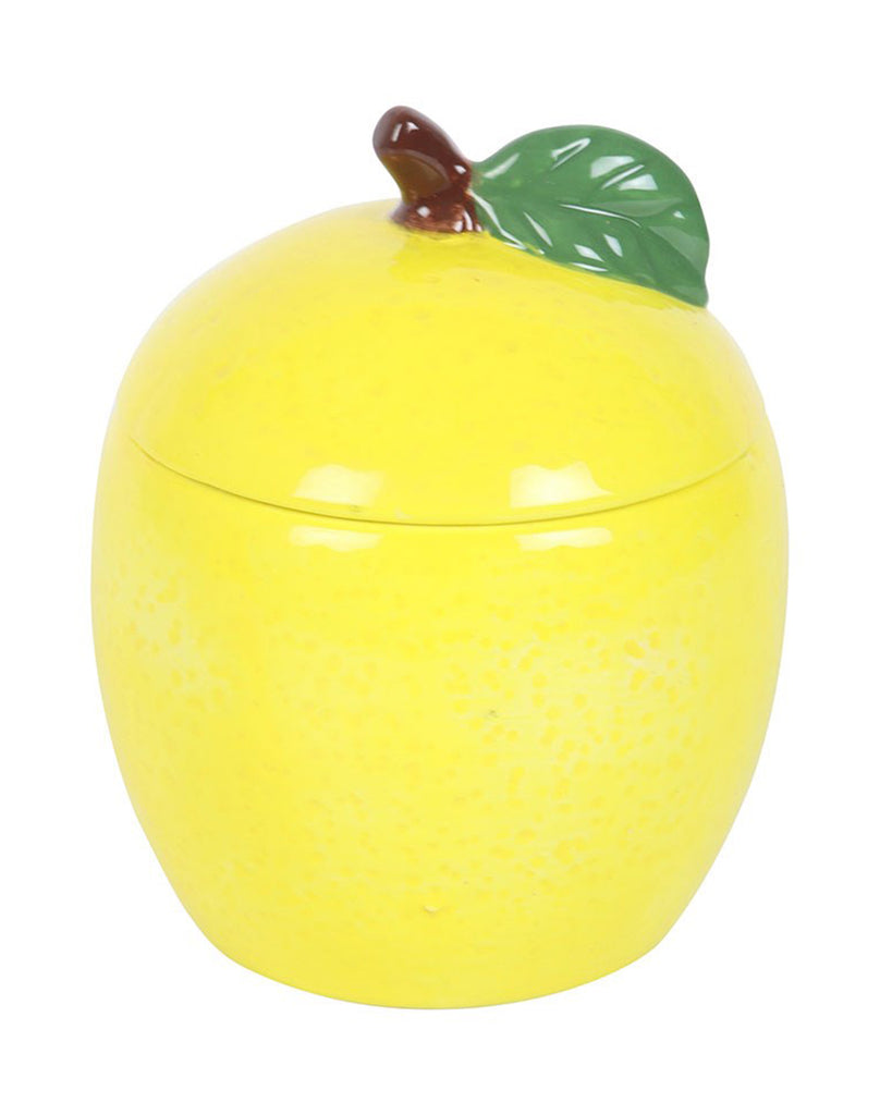 A front-facing view of the lemon-shaped candle jar with the lid on. The detailed ceramic leaf and stem on the lid add a whimsical touch.