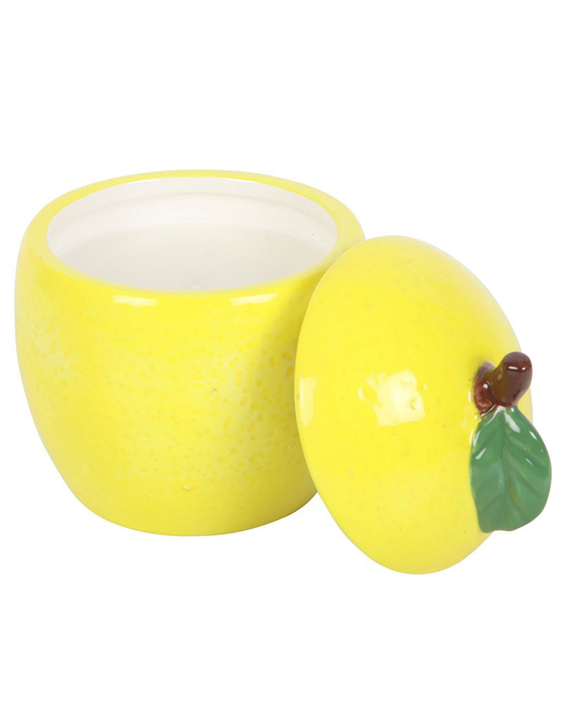 A ceramic lemon-shaped candle jar with its lid placed beside it. The bright yellow finish and realistic dimpled texture mimic a fresh lemon, making it a charming home accessory.