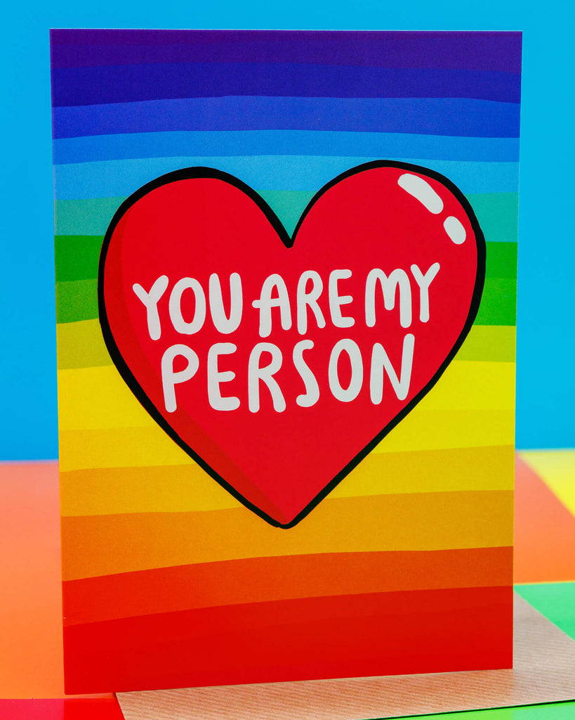 A colourful rainbow stripe A6 greeting card by Rebel Romance, featuring a red heart with the words "You Are My Person" in bold white text. The background has horizontal rainbow stripes from red to purple. Designed by UK illustrator Katie Abey, this vibrant and quirky card is perfect for expressing love, appreciation, or friendship. A fun, heartfelt design ideal for anniversaries, Valentine’s Day, or just because.