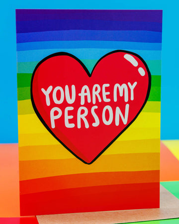 A colourful rainbow stripe A6 greeting card by Rebel Romance, featuring a red heart with the words "You Are My Person" in bold white text. The background has horizontal rainbow stripes from red to purple. Designed by UK illustrator Katie Abey, this vibrant and quirky card is perfect for expressing love, appreciation, or friendship. A fun, heartfelt design ideal for anniversaries, Valentine’s Day, or just because.